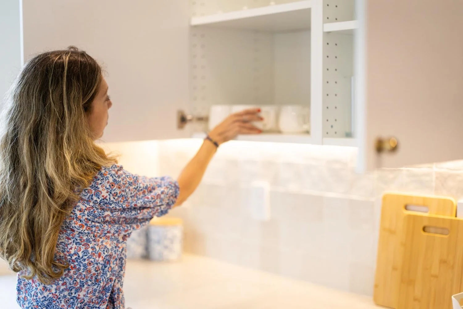 Adi placing mugs into a kitchen cabinet while setting up the home